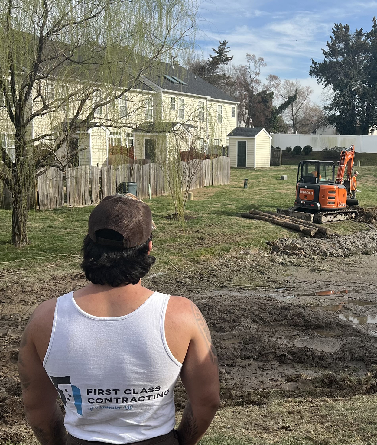 A man wearing a First Class Contracting shirt oversees construction in the backyard of a home